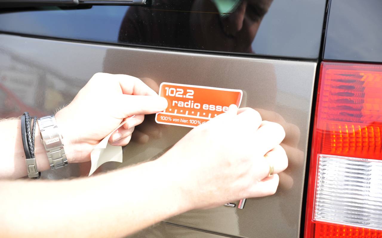 Hände eines Mannes kleben einen roten Radio Essen-Aufkleber hinten auf ein Auto.