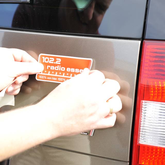 Hände eines Mannes kleben einen roten Radio Essen-Aufkleber hinten auf ein Auto.