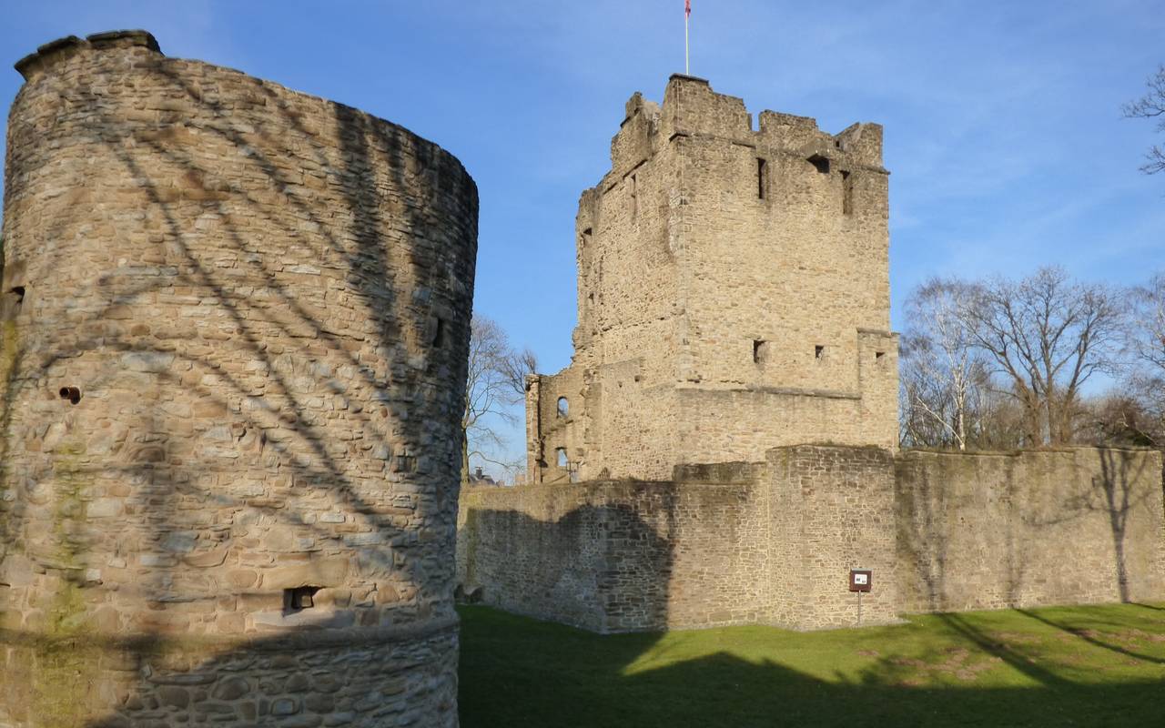 Die graue Burgruine in Burgaltendorf mit starken Mauern, Türmen und Wiesen drum herum.