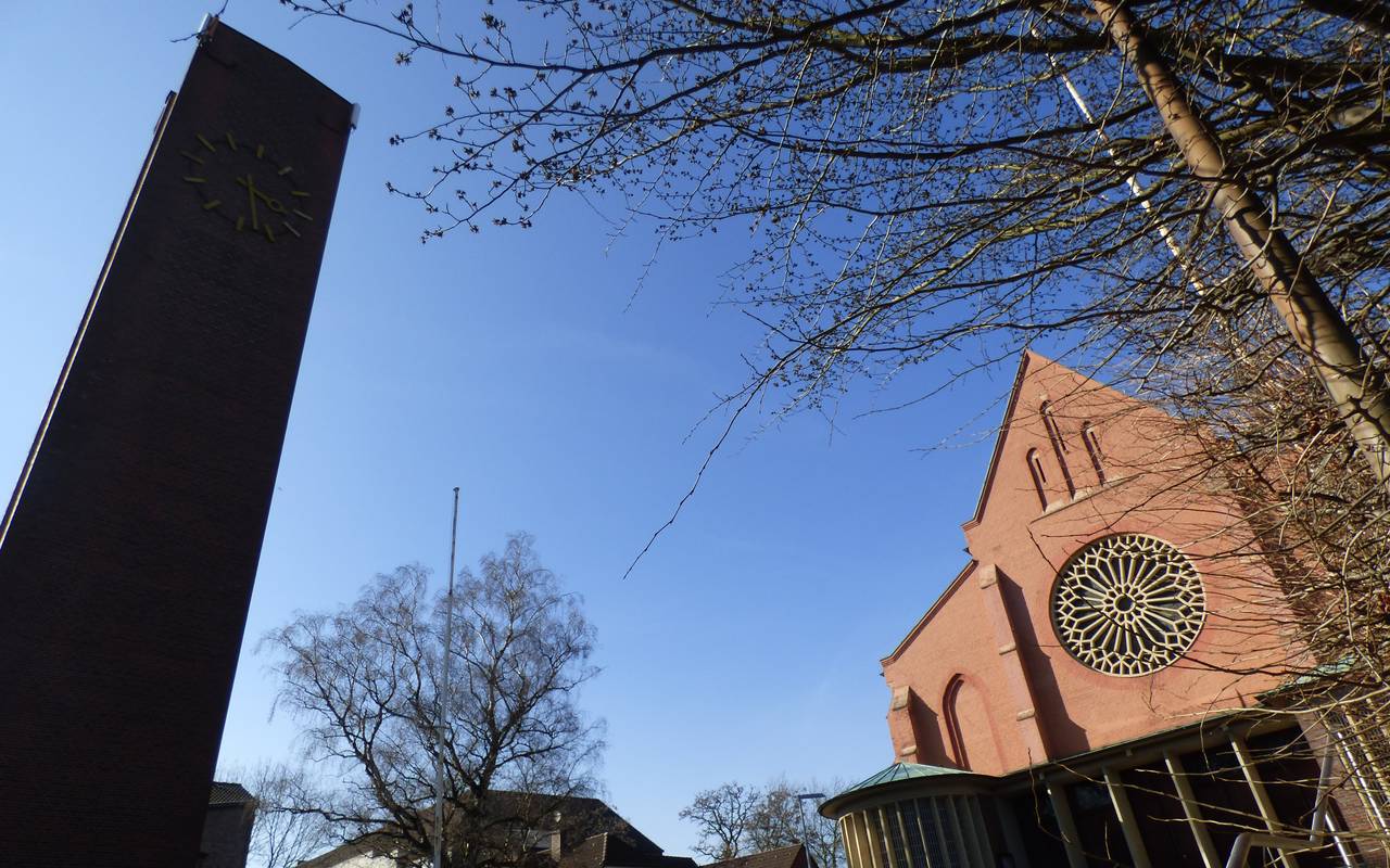 Mit rot-braunen Backsteinen gebaute Kirche mit großer Uhr und einem rechteckigen Turm.