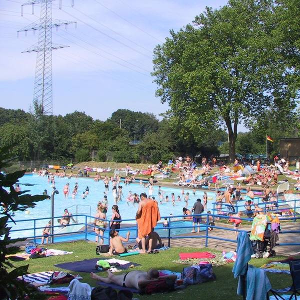 Das Schwimmbecken im Freibad Hesse in Essen Dellwig mit vielen Besuchern und drum herum die Liegewiesen.