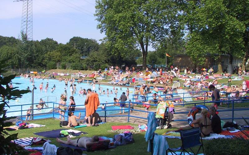 Das Schwimmbecken im Freibad Hesse in Essen Dellwig mit vielen Besuchern und drum herum die Liegewiesen.