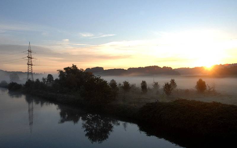 Die Ruhr bei Essen Überruhr fließt entlang an einem bewaldeten Ufer im Sonnenaufgang.