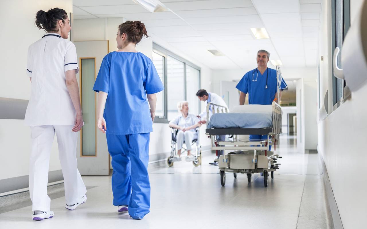 Ein Krankenhausflur mit Schwestern und Pflegern in blauen Sachen. Sie schieben Betten.