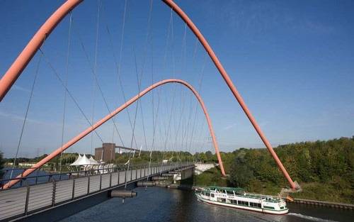 Ein Schiff der Weißen Flotte schippert über den Rhein-Herne-Kanal unter einer Brücke mit orangenen Bögen