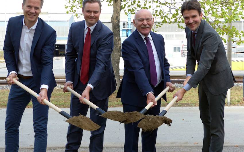 Vier Männer stehen mit Schaufeln an einer Baugrube und setzen symbolisch den ersten Spatenstich.