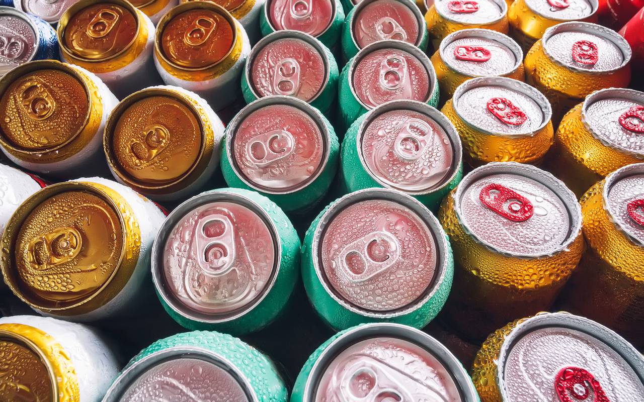 Metalldosen, gefüllt mit Bier auf Eiswürfeln im Minikühlschrank, Nahaufnahme. Viele Aluminiumdosen im Eis im offenen Kühlschrank. Tropfen Wasser auf eine kalte Getränkedose.