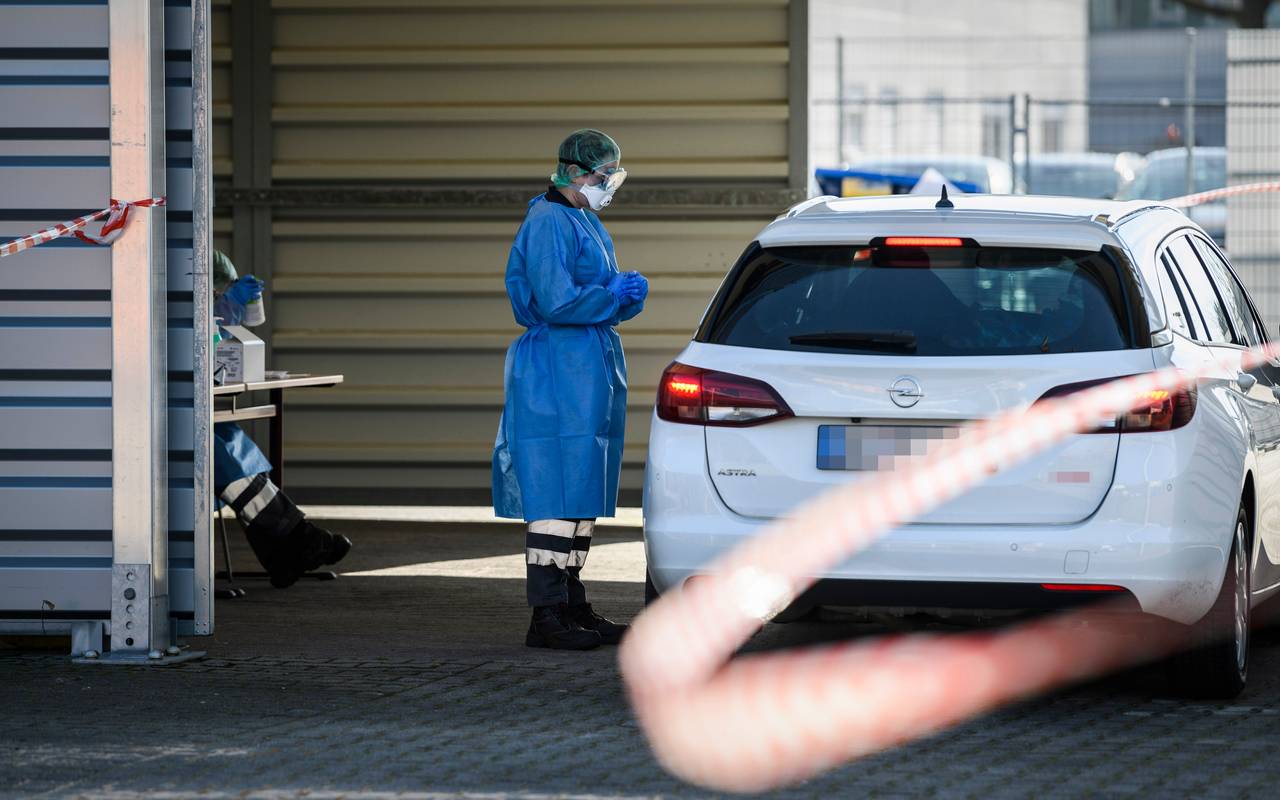 Ein DRK-Mitarbeiter in Schutzkleidung steht neben einem Auto in der provisorischen Halle der "Drive in"-Teststelle für Corona-Tests.