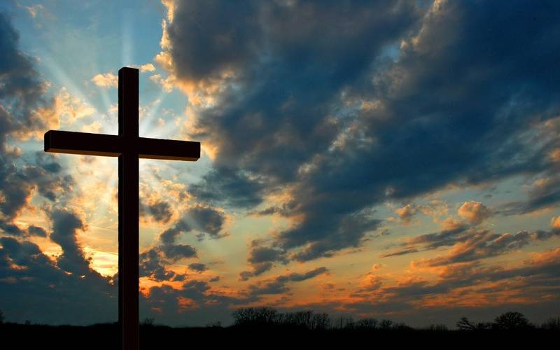Kreuz steht vor Himmel mit Sonnenstrahlen durch Wolken