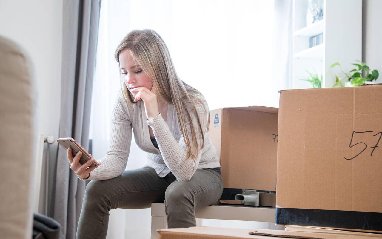 Eine Frau sieht zwischen Umzugskartons auf ein Handy