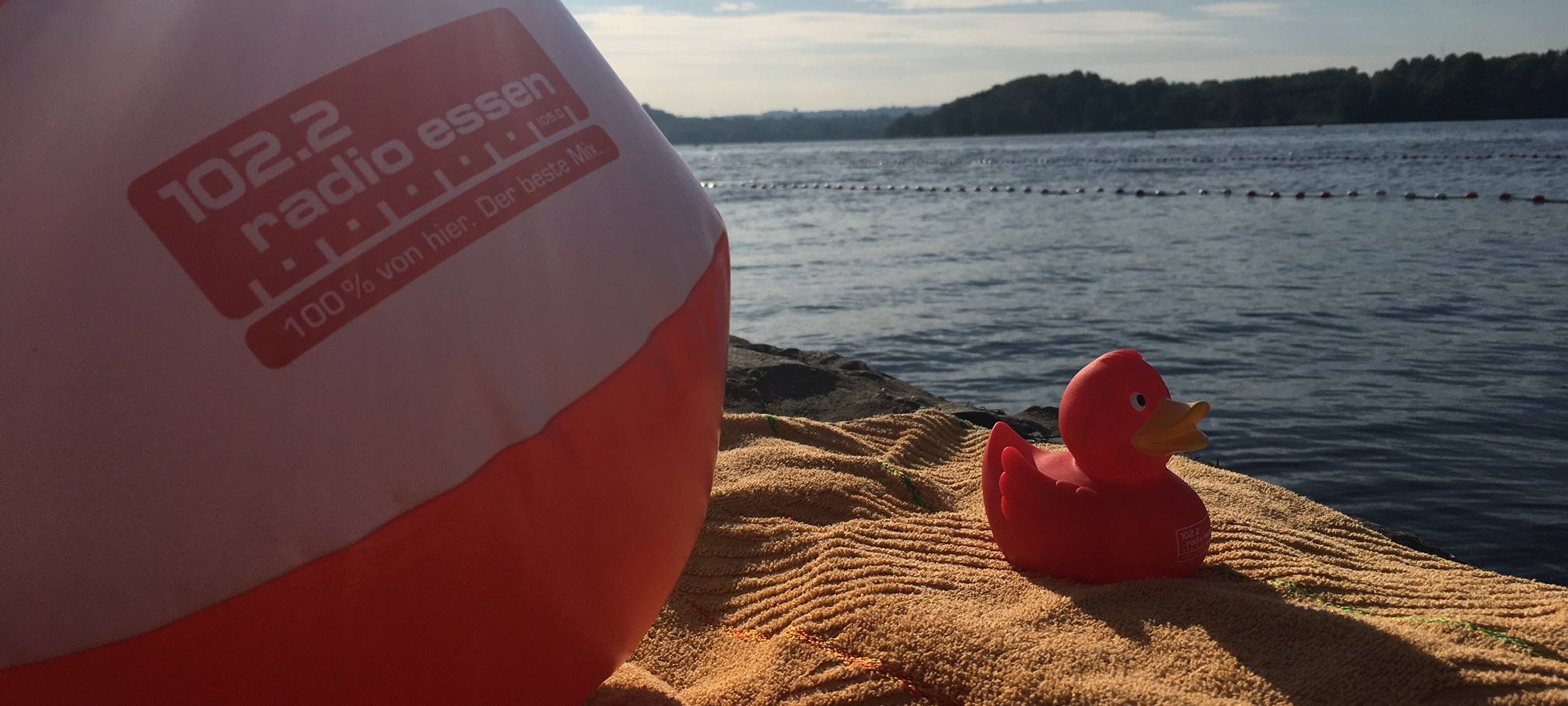 Radio Essen-Badeente Erna mit rot-weißem Radio Essen-Wasserball im Sand am Baldeneysee