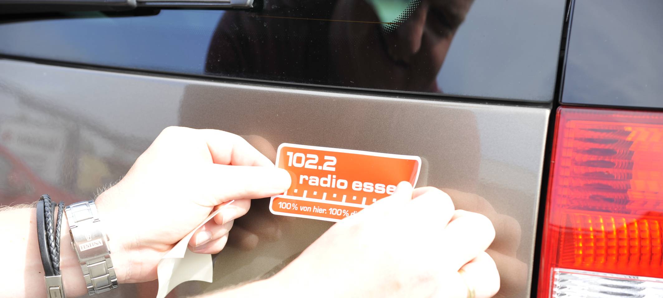 Hände eines Mannes kleben einen roten Radio Essen-Aufkleber hinten auf ein Auto.