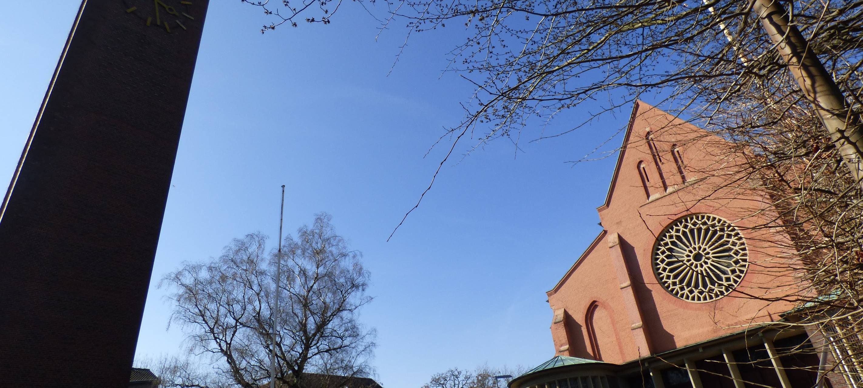 Mit rot-braunen Backsteinen gebaute Kirche mit großer Uhr und einem rechteckigen Turm.