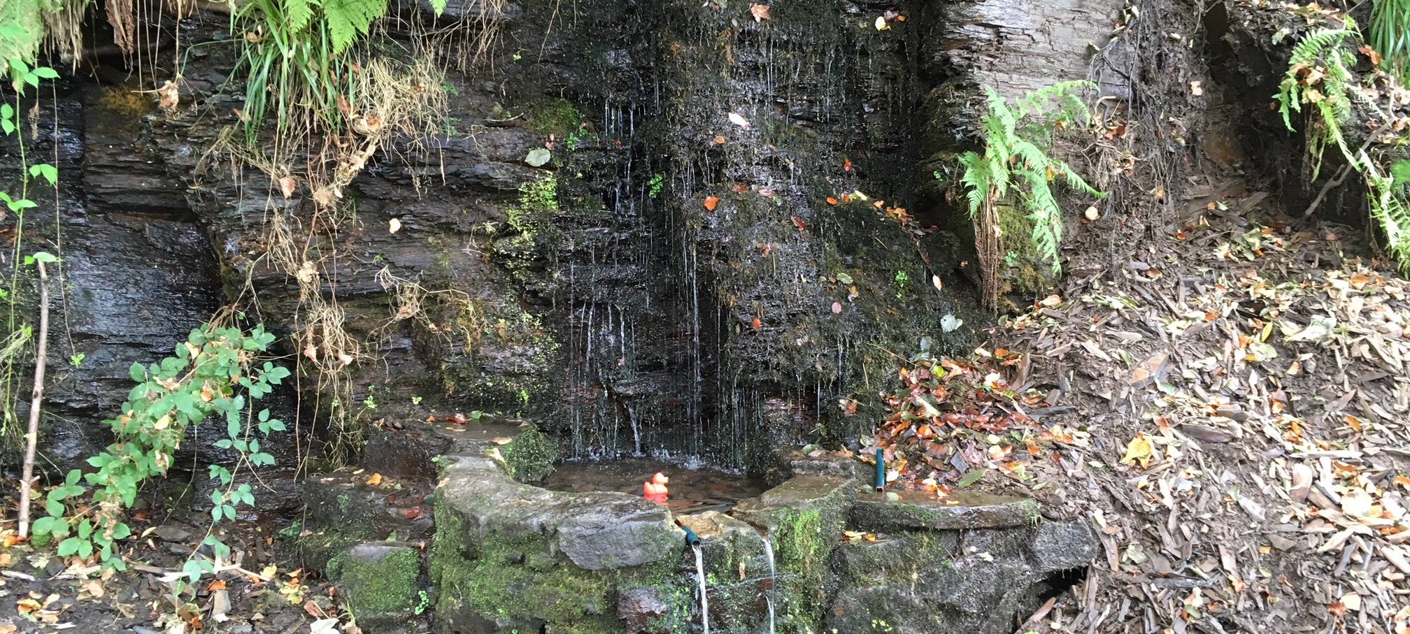 Die kleine rote Radio Essen-Badeente Erna schwimmt in einem runden Felsvorsprung in den Wasser aus der Felsenquelle in Kettwig fließt.