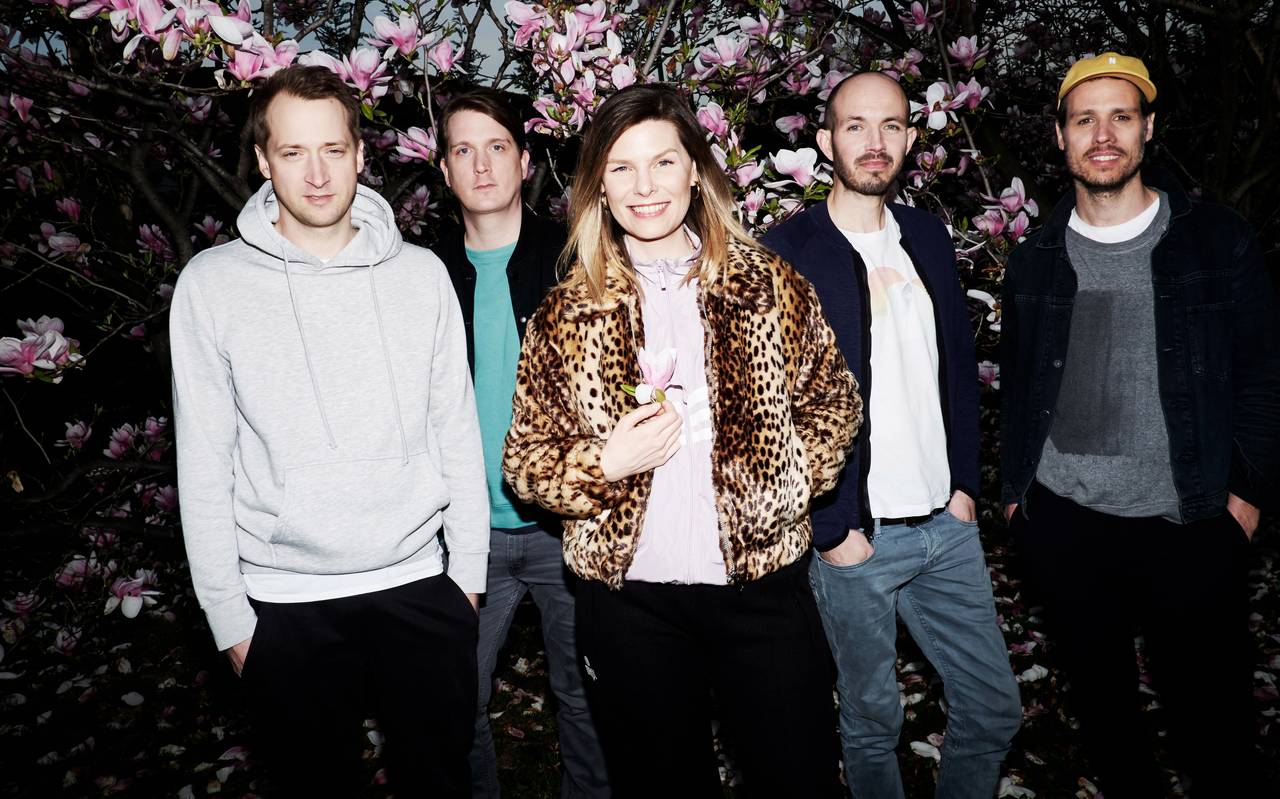 Die Band Juli mit vier Männern und der Frontfrau in der Mitte vor einem Busch mit rosa Blüten.