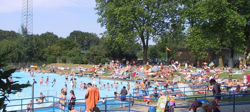 Das Schwimmbecken im Freibad Hesse in Essen Dellwig mit vielen Besuchern und drum herum die Liegewiesen.
