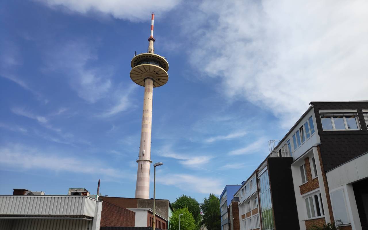Der Funkturm in Holsterhausen ist eine schmale graue Säule mit gläsernem Rundturm und orange-weiß gestreifter Spitze.