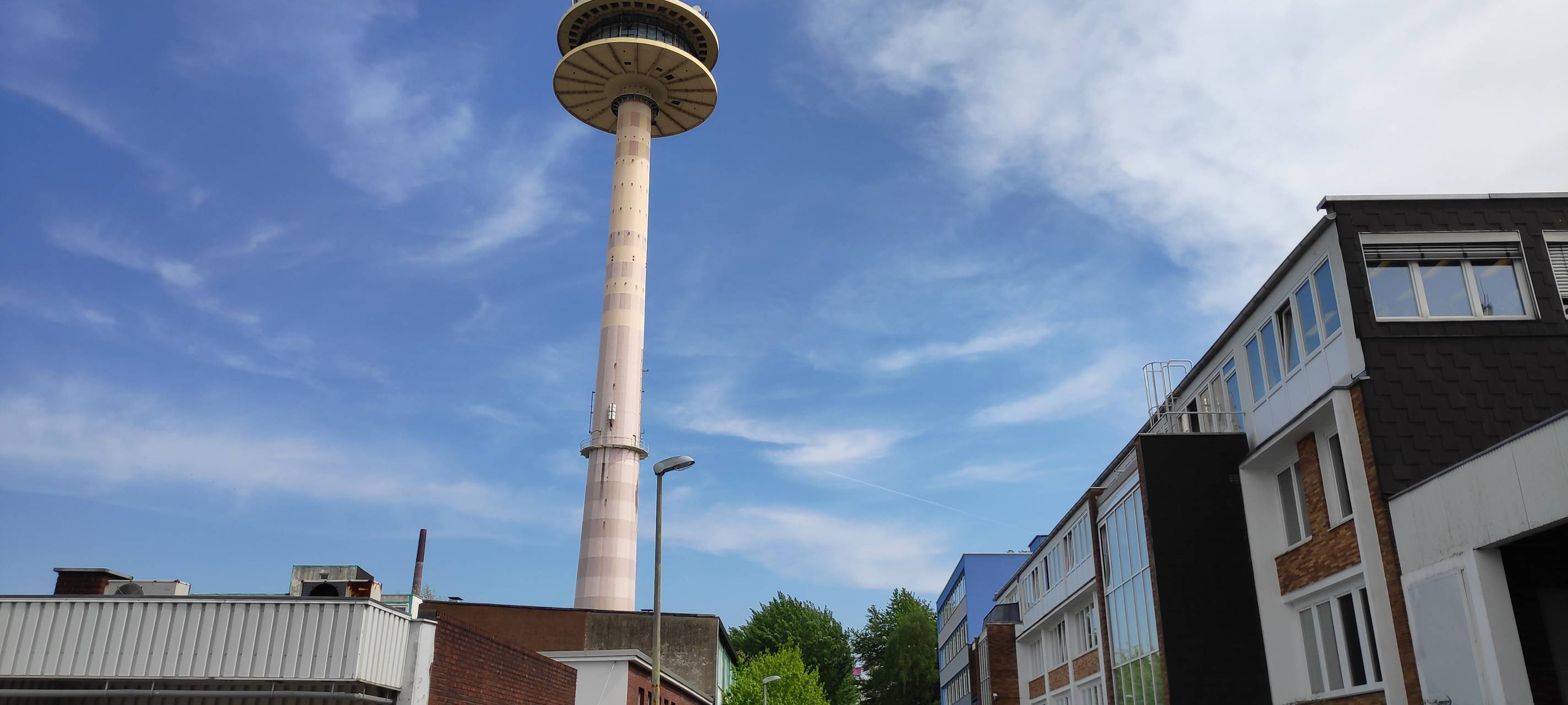 Der Funkturm in Holsterhausen ist eine schmale graue Säule mit gläsernem Rundturm und orange-weiß gestreifter Spitze.