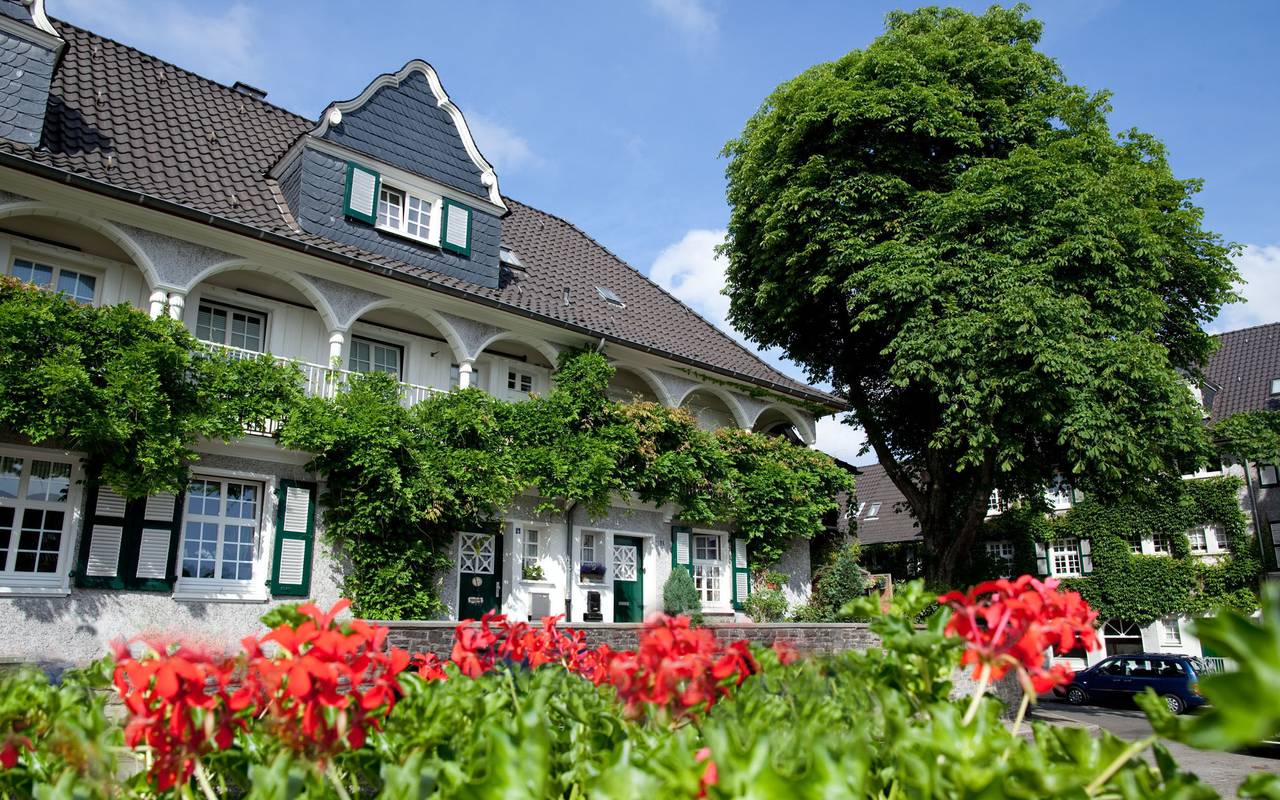 Klassisches weißes Haus mit Spitzdach, geschwungenen Balkonen und viel grün und Blumen an der Margarethenhöhe in Essen.