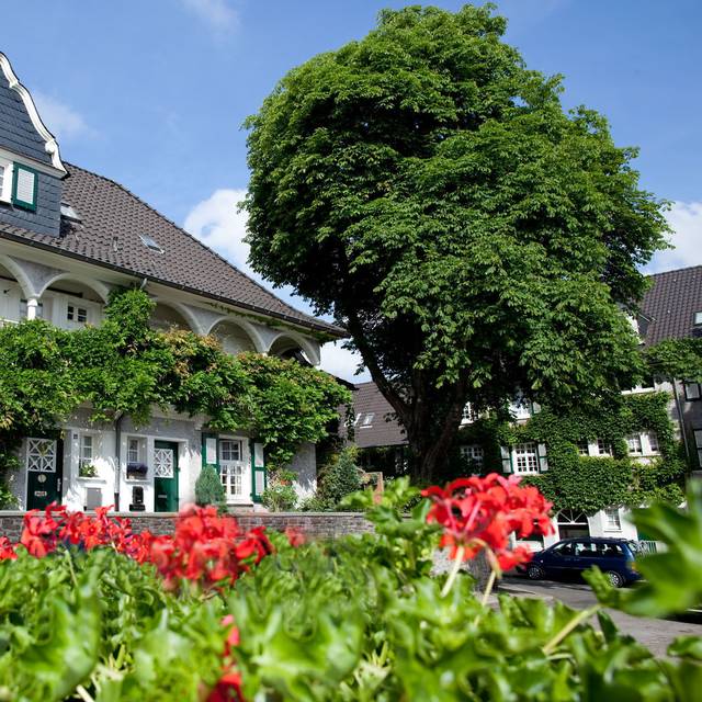 Klassisches weißes Haus mit Spitzdach, geschwungenen Balkonen und viel grün und Blumen an der Margarethenhöhe in Essen.