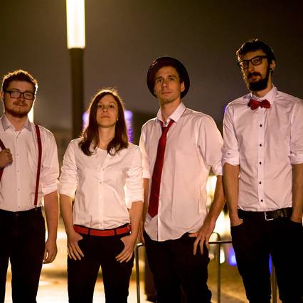 Drei Jungs und eine Frau in weißen Hemden und schwarzen Hosen vor einer Stadt-Skyline.