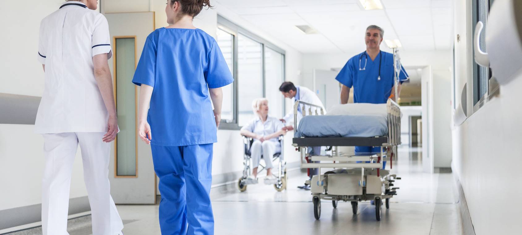 Ein Krankenhausflur mit Schwestern und Pflegern in blauen Sachen. Sie schieben Betten.