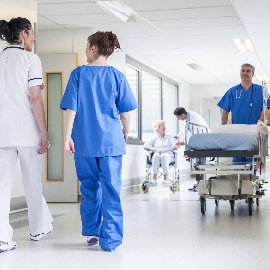 Ein Krankenhausflur mit Schwestern und Pflegern in blauen Sachen. Sie schieben Betten.