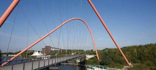 Ein Schiff der Weißen Flotte schippert über den Rhein-Herne-Kanal unter einer Brücke mit orangenen Bögen