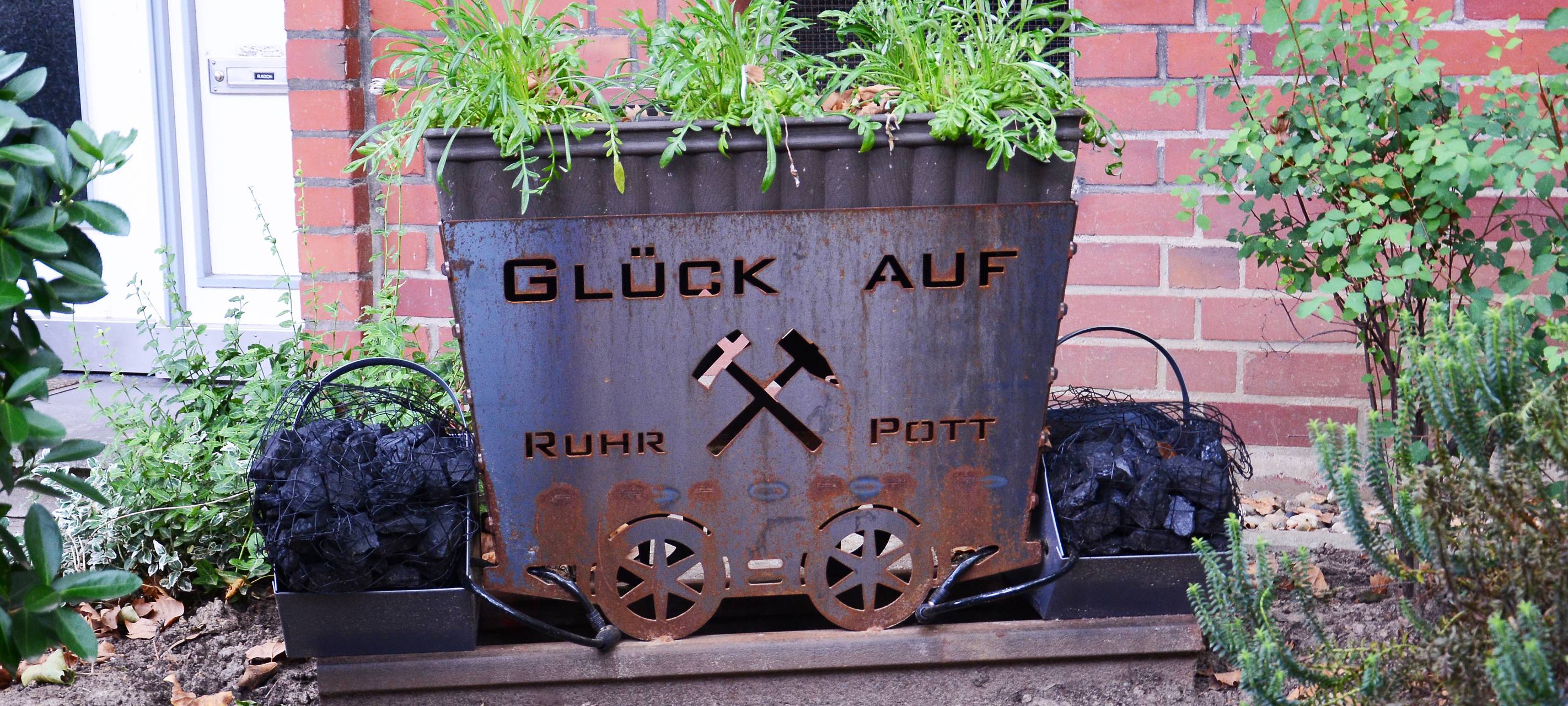 Eine kleine Lore mit Blumen bepflanzt steht in einem Vorgarten in Steele