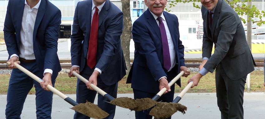 Vier Männer stehen mit Schaufeln an einer Baugrube und setzen symbolisch den ersten Spatenstich.