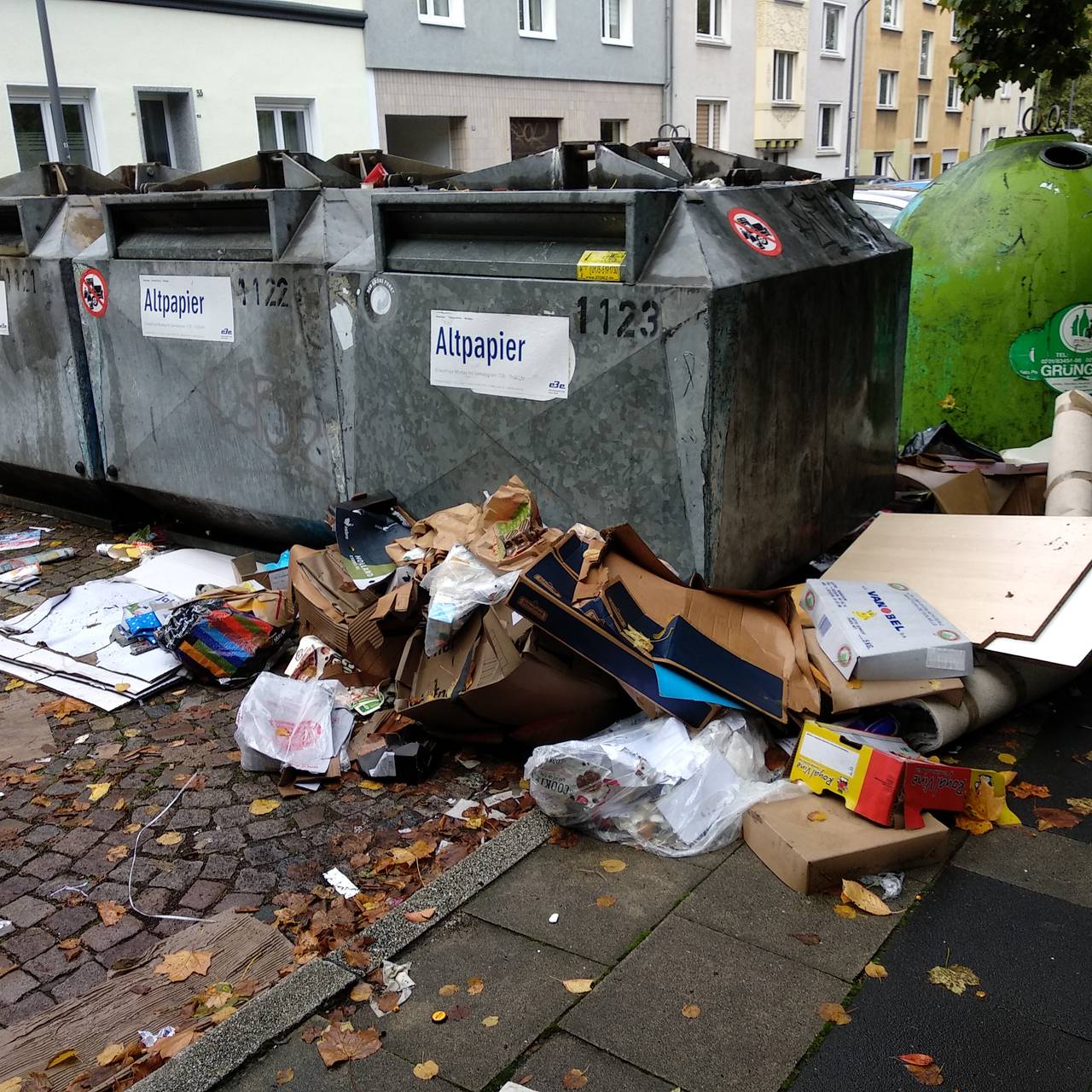 Container, daneben liegt viel Müll auf dem Boden: Kartons, Pappe und auch alte Teppiche.