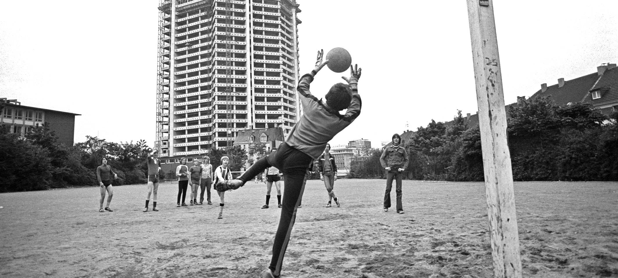 großer Rohbau vom Rathaus; im Vordergrund ein Fußballfeld mit Fußballspielern und einem Tor