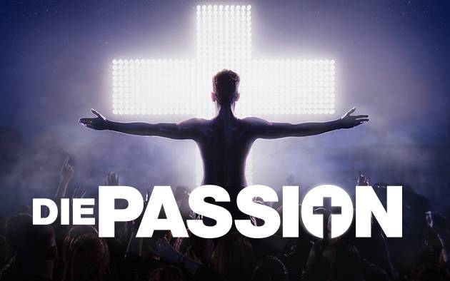 Teaserbild für die Show Passion; abgedunkelte Person steht mit ausgebreiteten Armen vor einem weiß leuchtenden Kreuz