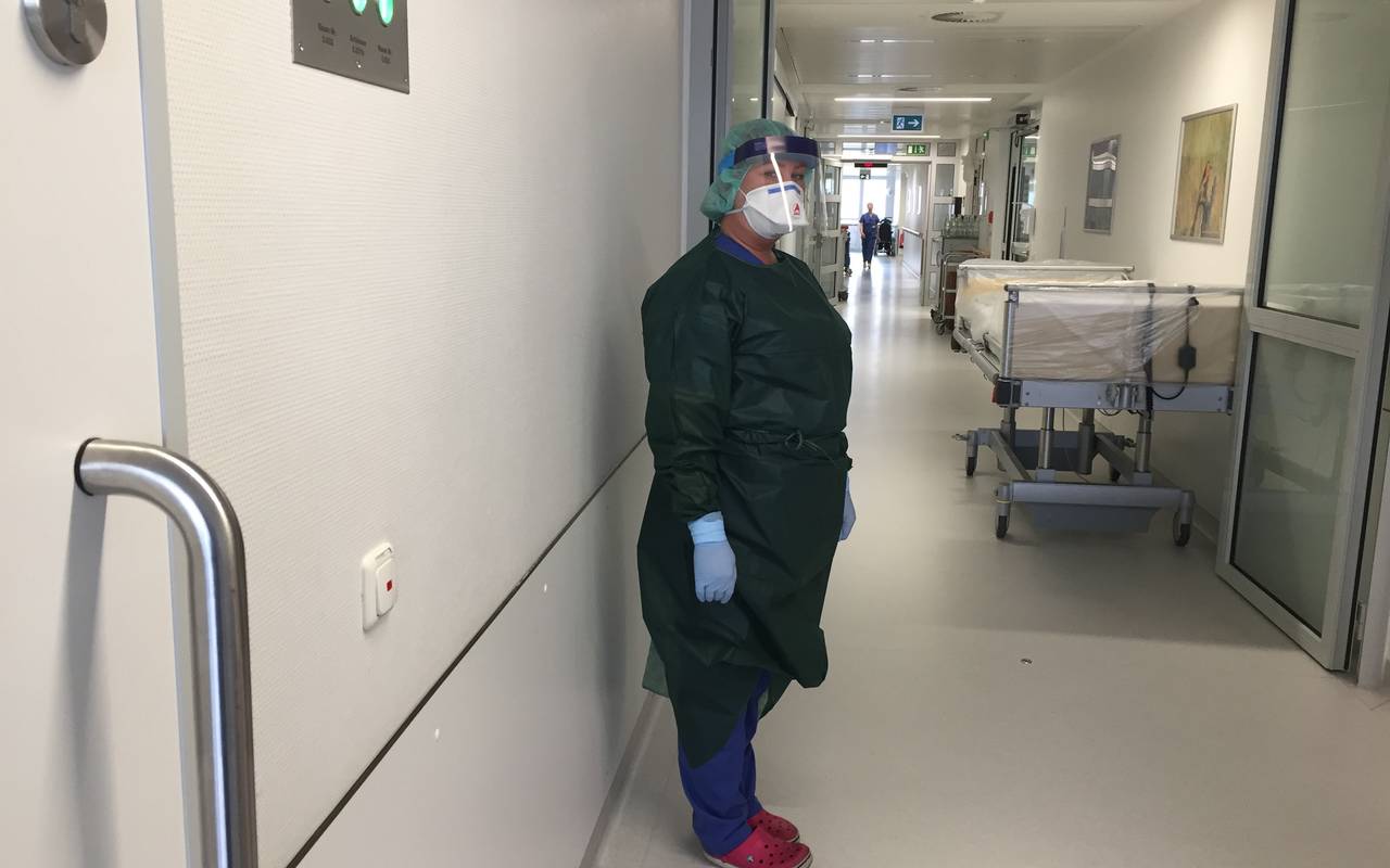 Frau im grünen Schutzanzug und mit Mundschutz auf einer Krankenhausstation