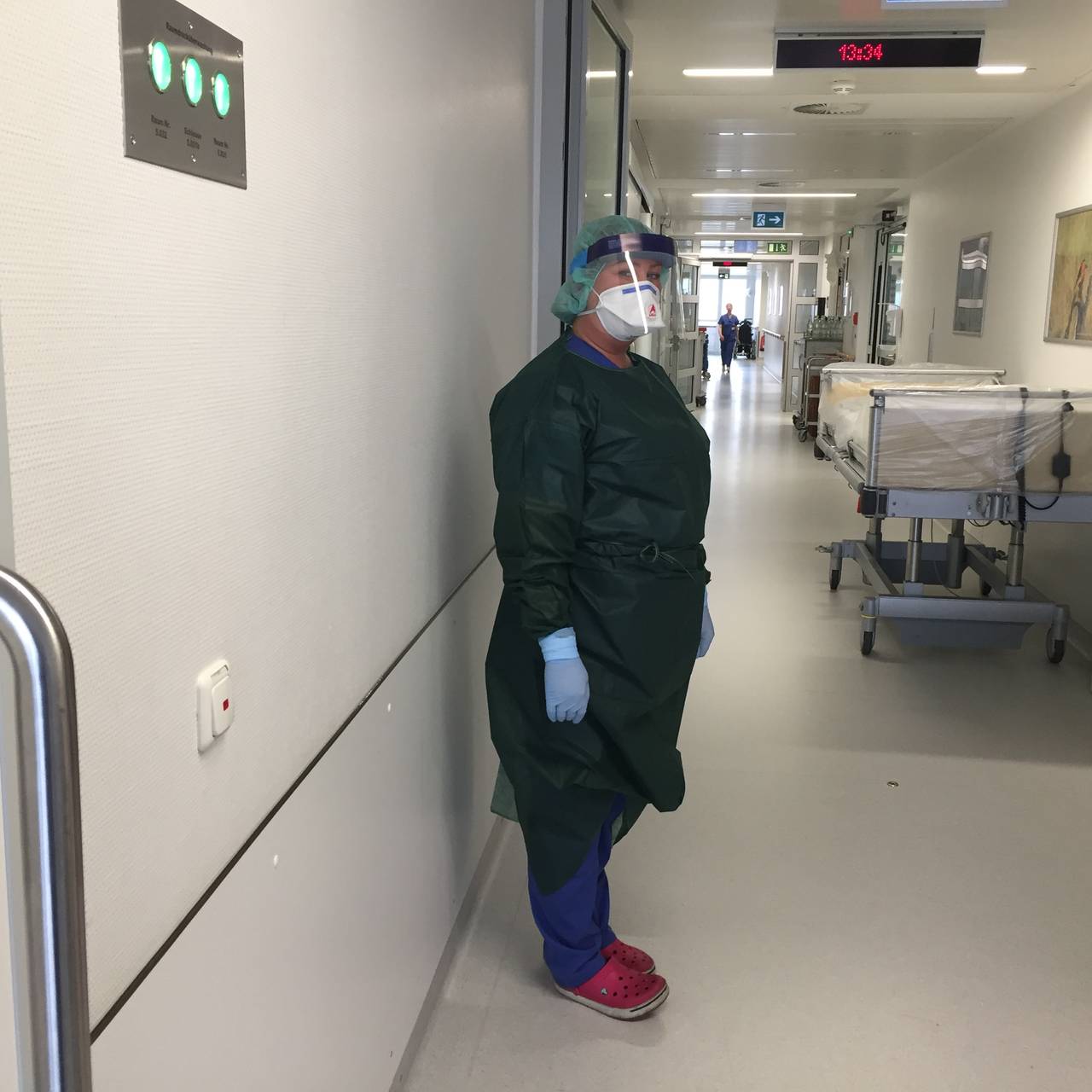 Frau im grünen Schutzanzug und mit Mundschutz auf einer Krankenhausstation