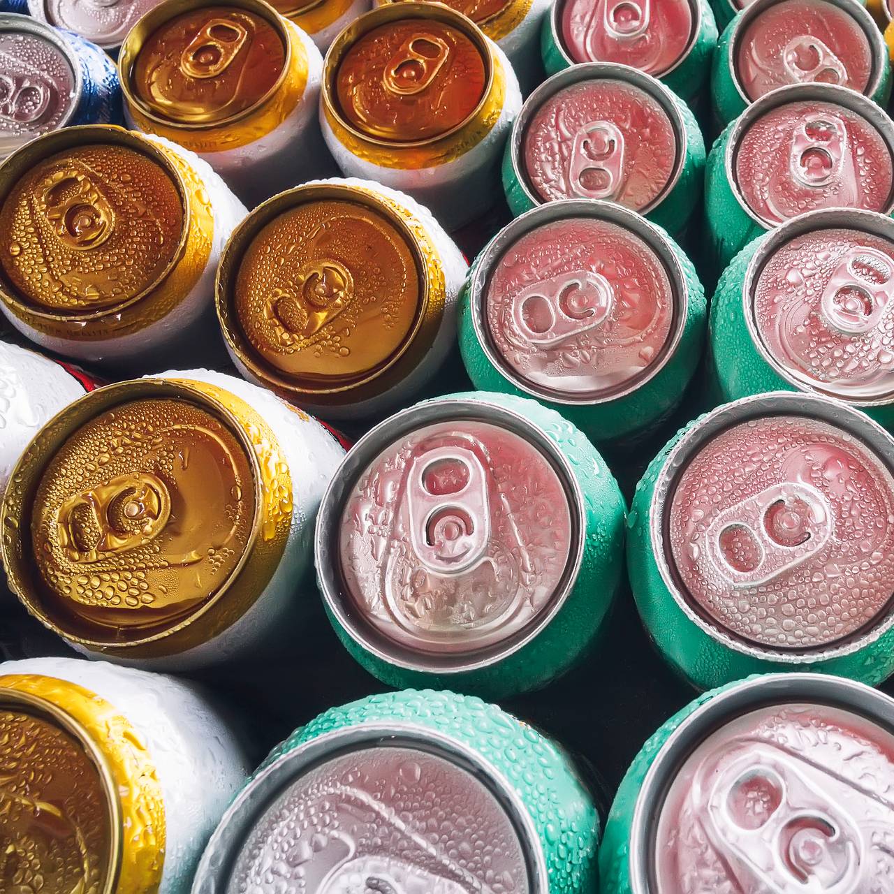 Metalldosen, gefüllt mit Bier auf Eiswürfeln im Minikühlschrank, Nahaufnahme. Viele Aluminiumdosen im Eis im offenen Kühlschrank. Tropfen Wasser auf eine kalte Getränkedose.