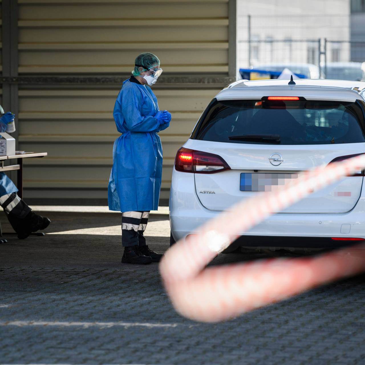 Ein DRK-Mitarbeiter in Schutzkleidung steht neben einem Auto in der provisorischen Halle der "Drive in"-Teststelle für Corona-Tests.