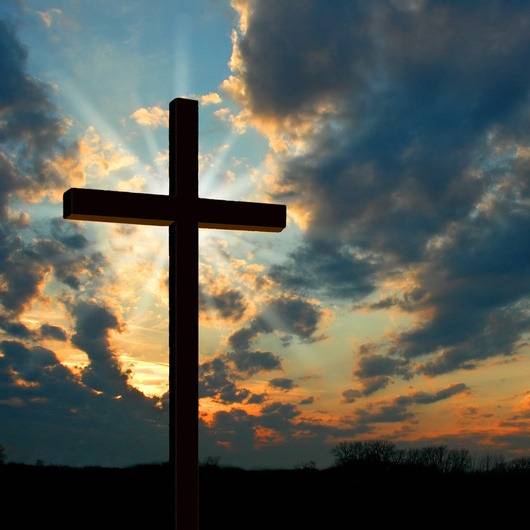 Kreuz steht vor Himmel mit Sonnenstrahlen durch Wolken