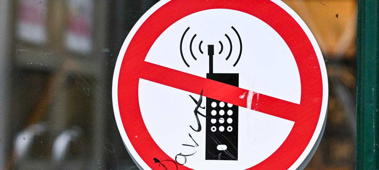 Ein Schild mit einem durchgestrichenen Handy-Symbol weist in einer Schule auf das Handyverbot hin.