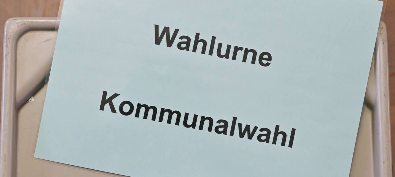 Ein Zettel mit der Aufschrift "Wahlurne Kommunalwahl" liegt auf einer Wahlurne in einem Wahllokal.