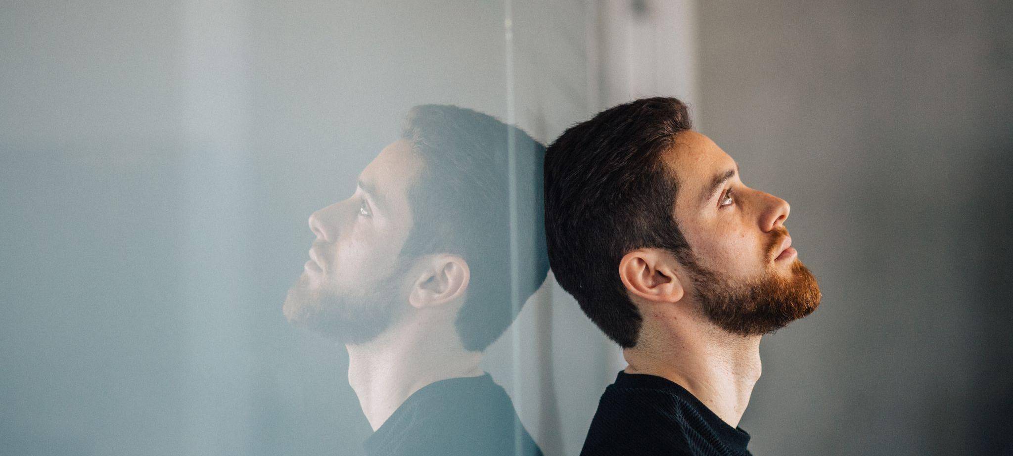 Ein junger Mann lehnt nachdenklich an einer Glaswand