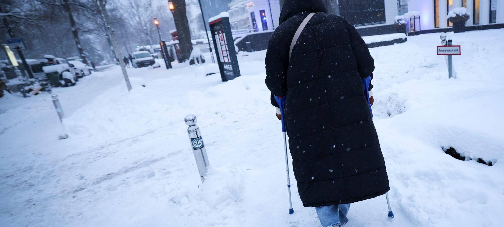 Ein Frau geht auf Eis mit Krücken und Spikes unter ihren Schuhen