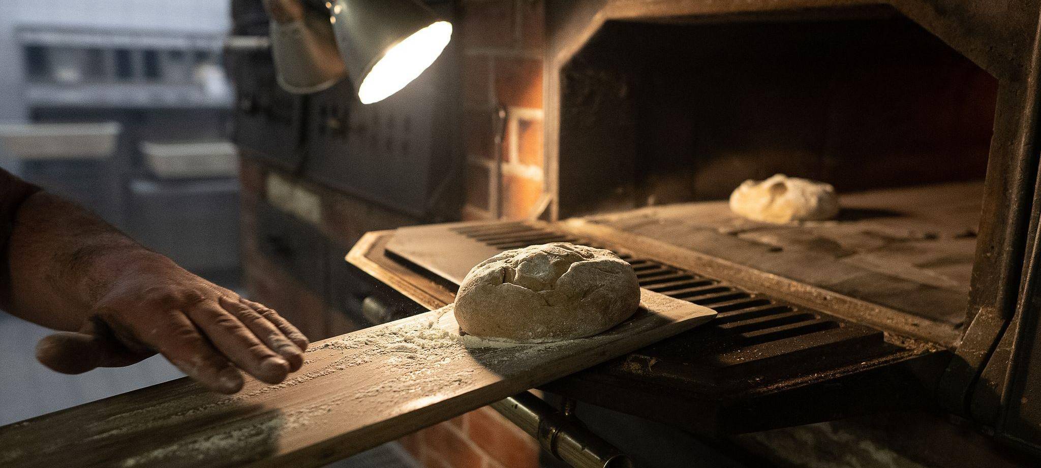 Teig wird auf einem Brotschieber in einen Ofen geschoben
