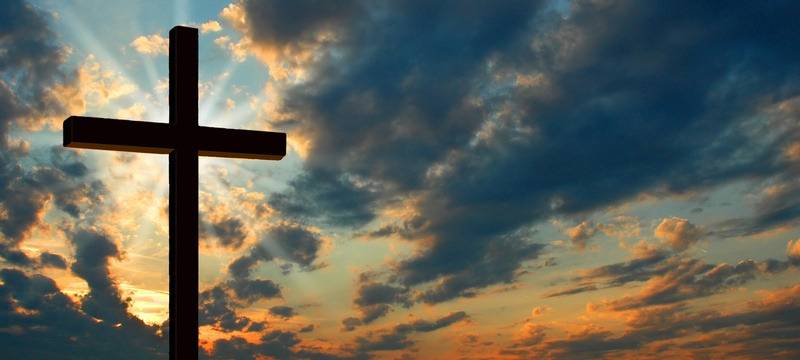 Kreuz steht vor Himmel mit Sonnenstrahlen durch Wolken