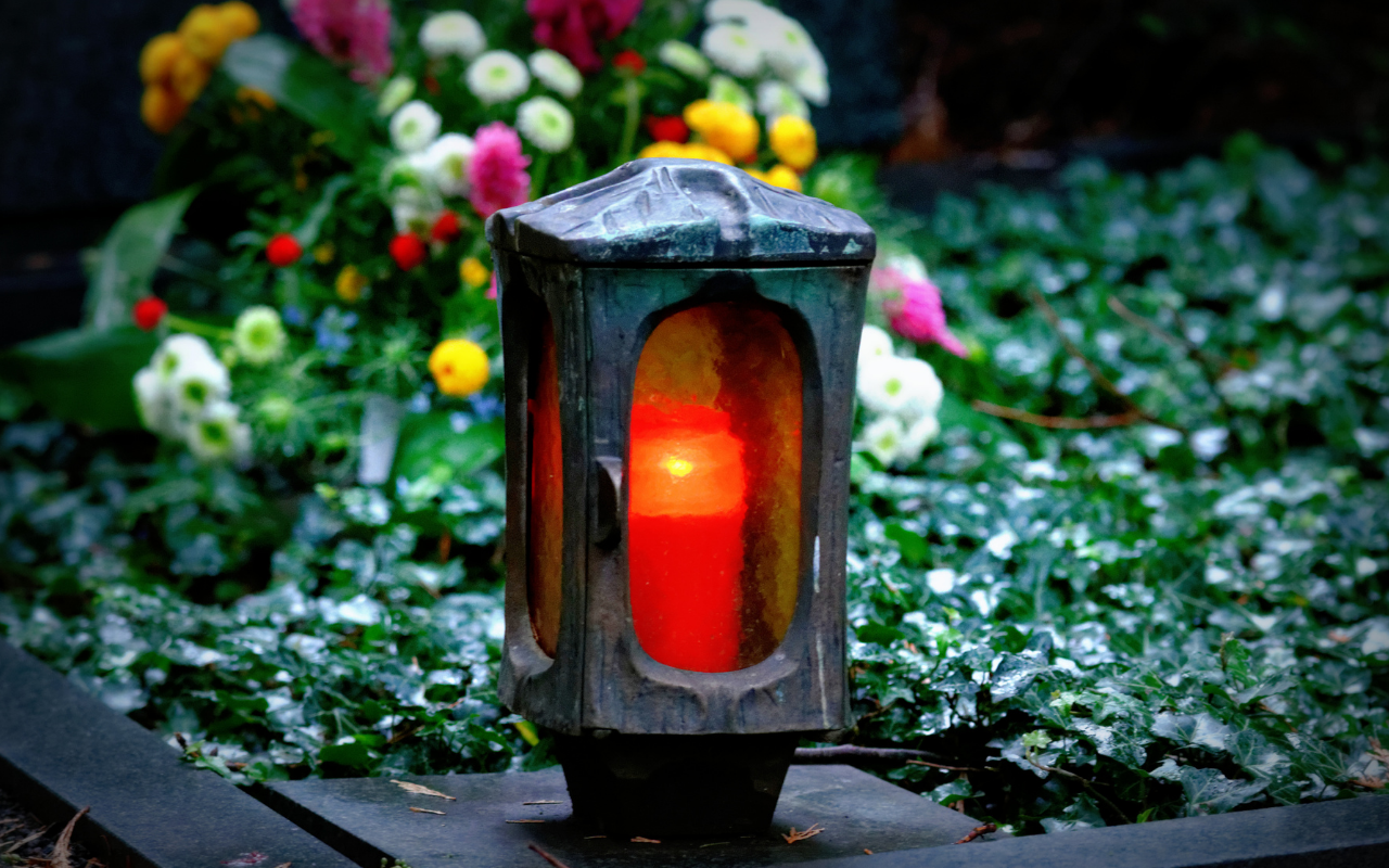 Symbolbild: Grablichter mit angezündeter roter Kerze.
