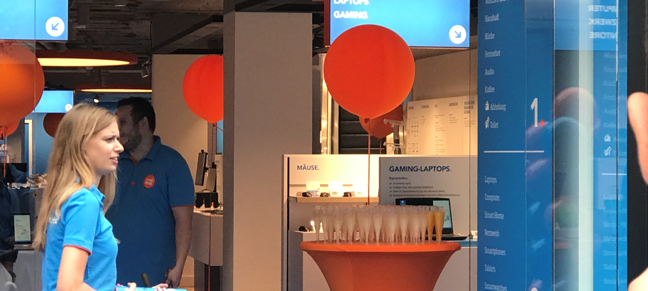 Am Eingang des blau gefärbten Geschäftes von Coolblue steht ein orangefarbiger Tisch für den Sektempfang